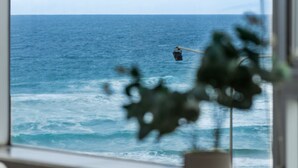 Une vue sur l’océan, aperçue à travers une fenêtre, avec un vase placé sur une table au premier plan.