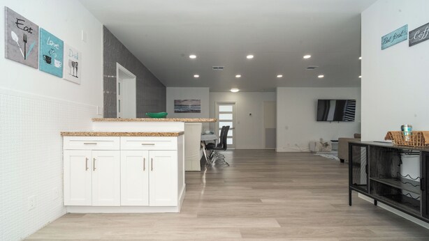 Una cocina moderna con armarios blancos, encimera de granito y un comedor con una silla y una mesa.