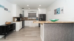 Una cocina moderna con armarios blancos, encimera de granito y un refrigerador de acero inoxidable.