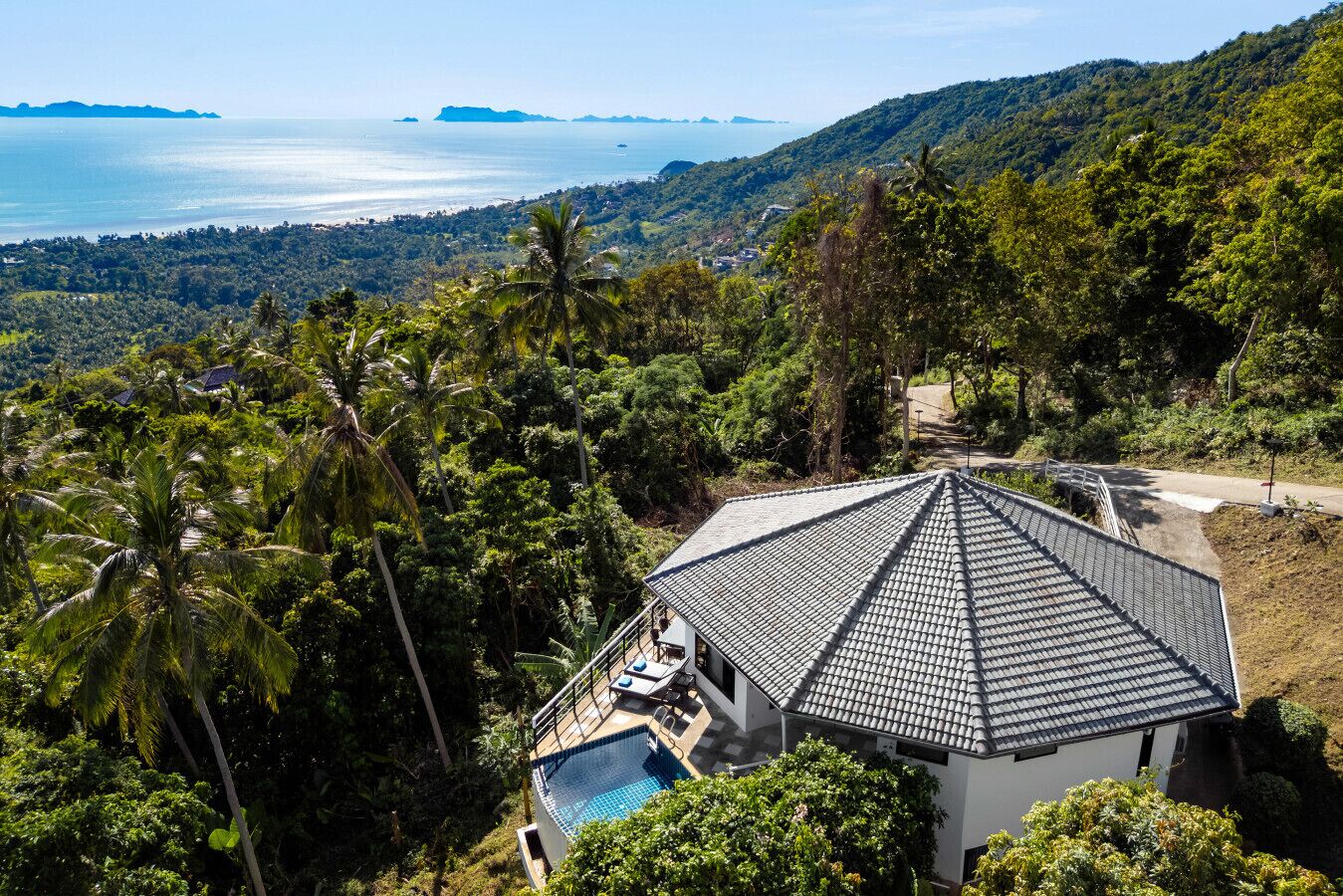 Una casa con techo de tejas, rodeada de abundante vegetación y vistas al mar.