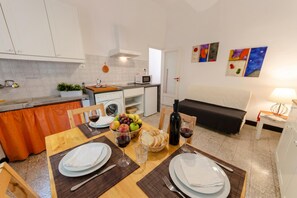 A compact kitchen with a microwave, toaster, and sink. A dining table is set with plates, glasses, and a fruit basket.
