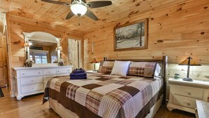 A cozy bedroom with a wooden ceiling, a bed with a plaid bedspread, a dresser, a nightstand, and a ceiling fan. - Rustic Cabin with Long Range Mountain Views - Hot Tub - Fire Pit (Blue Ridge)