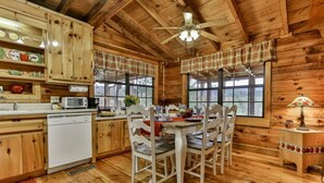A wooden cabin interior with a kitchen and dining area, featuring wooden cabinets, a dining table with chairs, and a ceiling fan. - Rustic Cabin with Long Range Mountain Views - Hot Tub - Fire Pit (Blue Ridge)