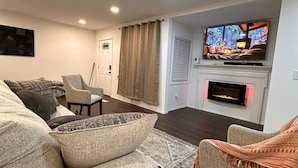 Een woonkamer met een bank, fauteuil en een flatscreen televisie boven een open haard.