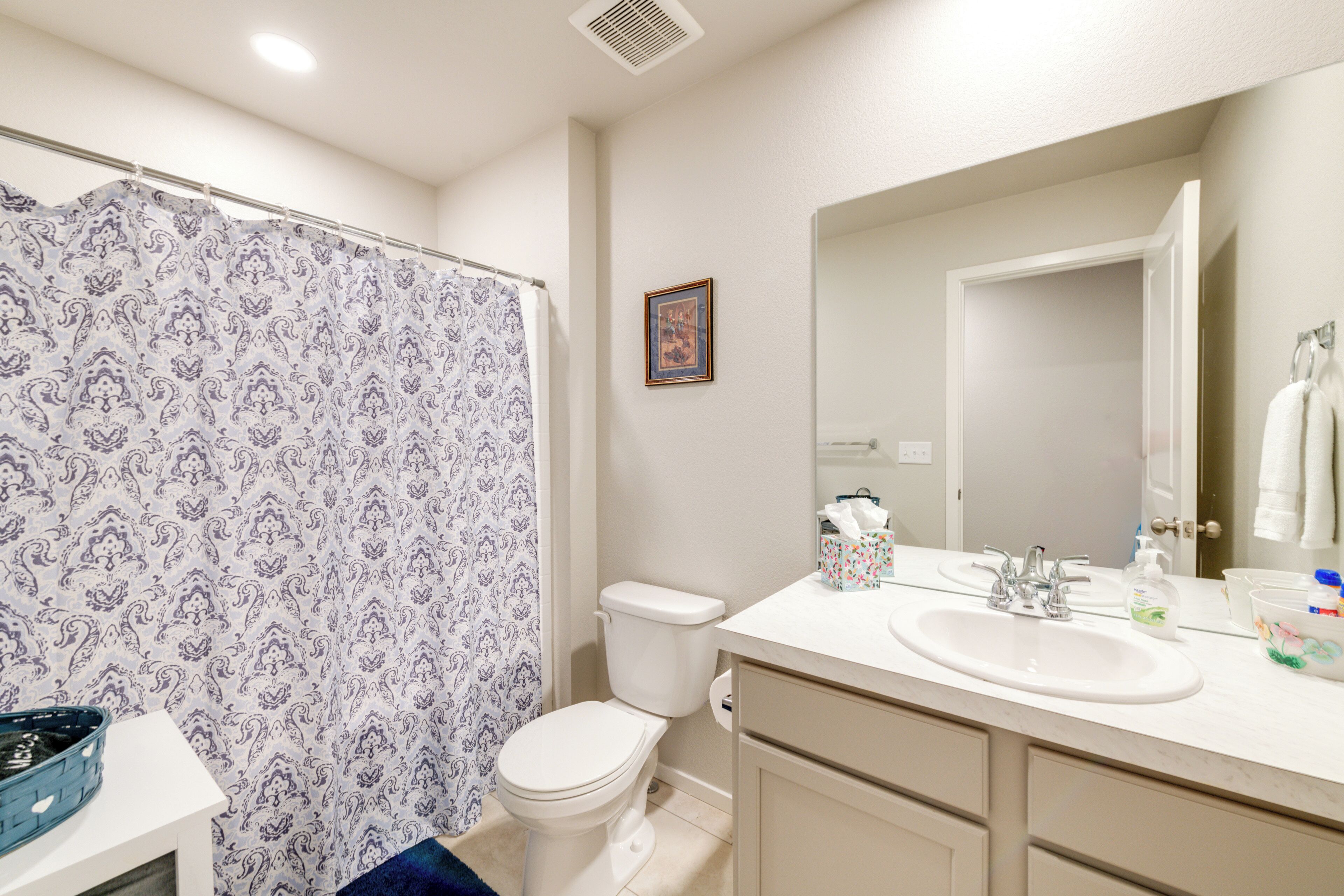 A bathroom with a shower curtain, toilet, sink, and cabinets.