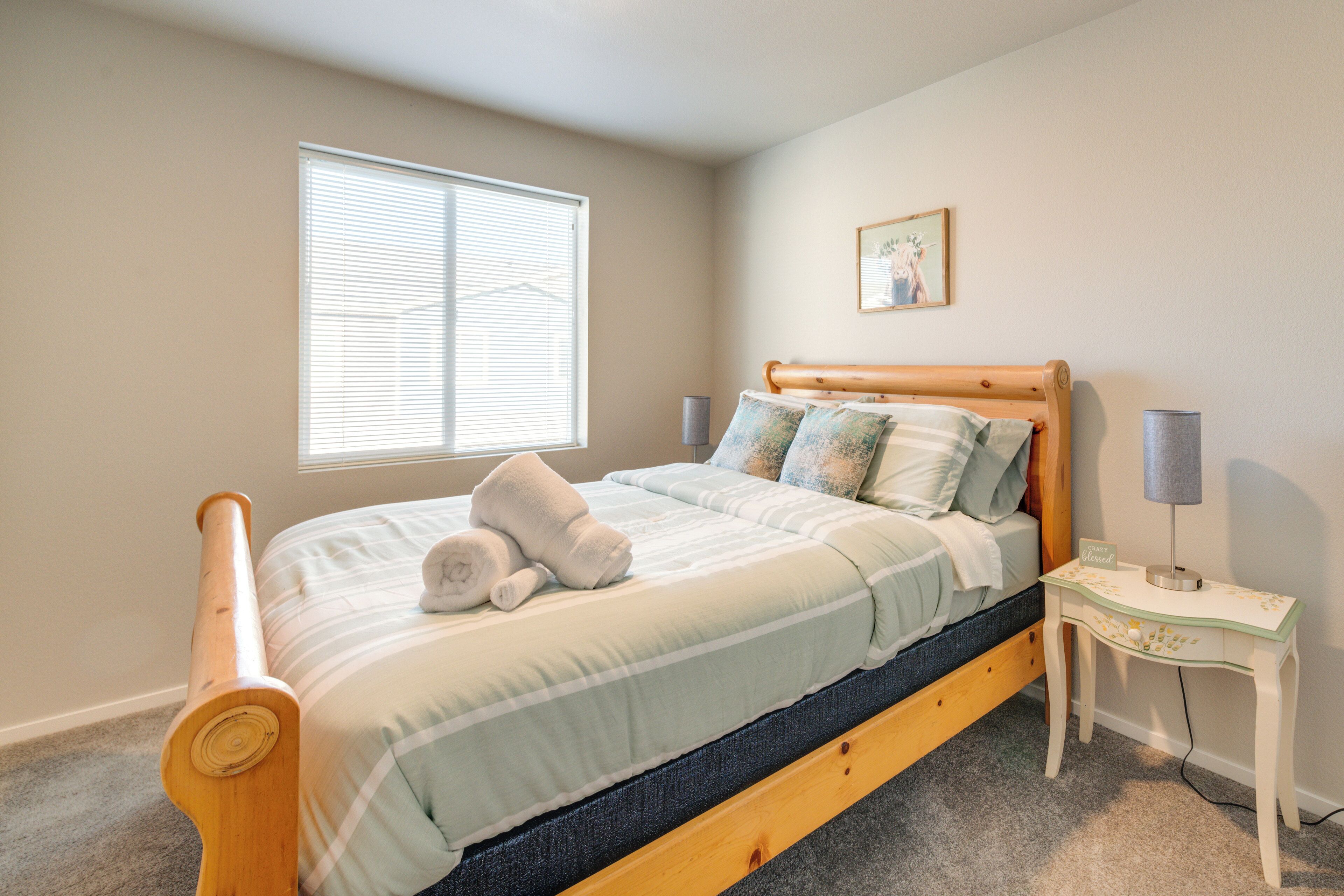 A bedroom with a wooden bed, a bedside table with lamps, and a window with blinds.