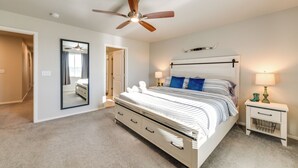 Ein Schlafzimmer mit einem Bett, einem Deckenventilator, einem Nachttisch mit Lampe und einem Spiegel.