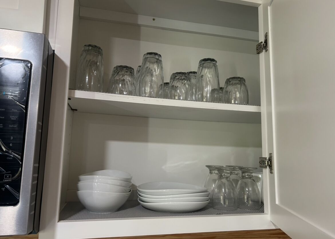 Ett köksskåp med hyllor där glasburkar och vita skålar förvaras.
