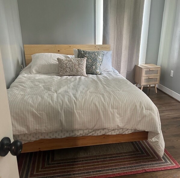Un lit bien fait, avec une tête de lit en bois, une table de chevet et un tapis à motifs sur un plancher en bois.