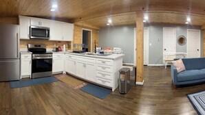 Una cocina moderna con gabinetes blancos, electrodomésticos de acero inoxidable y una zona de comedor con sofá azul y piso de madera.
