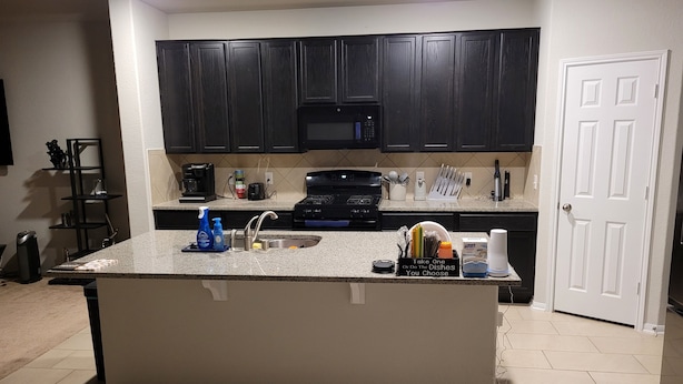 A kitchen with dark cabinets, a granite countertop, a built-in microwave, and a sink.