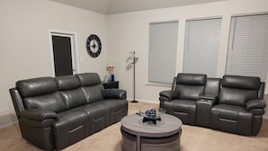 A living room with two black leather sofas, a round coffee table, a wall clock, and a floor lamp.