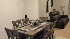 A dining area with a table and chairs, a sofa, and a wall with the word "HOME" spelled out.