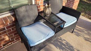 A wicker patio chair with a glass table and light blue cushions.
