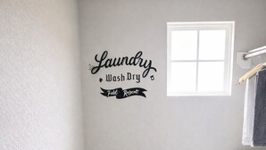 A laundry room with a wall-mounted washer and dryer, a small window, and a grey laundry basket.