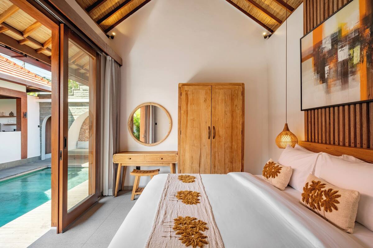 Une chambre avec un grand lit, une armoire en bois, un bureau et une vue sur une piscine.