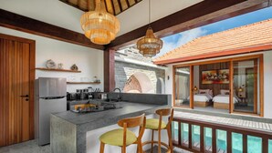 A modern kitchen with a large island, wooden chairs, and a view of a pool. - Casa Bojo & Casa Bella Uluwatu (Pecatu)