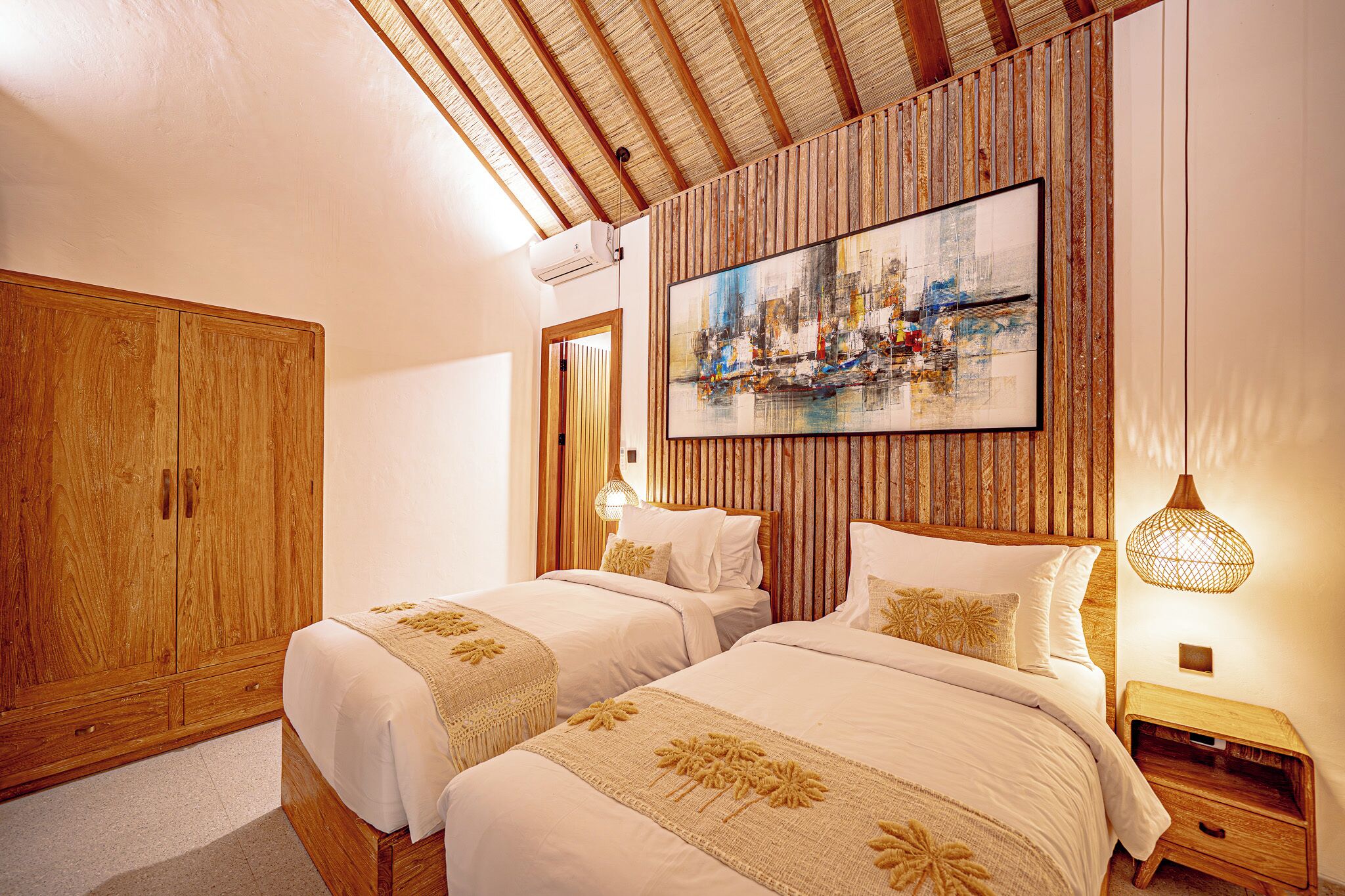 Quarto com duas camas, cabeceira de madeira, uma pintura grande e uma mesa de cabeceira com abajur.