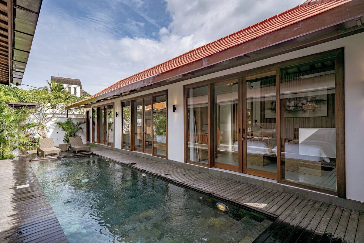 Un hôtel moderne doté d’une piscine, de grandes portes vitrées et d’une terrasse en bois.
