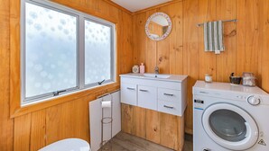 Un baño de madera pequeño y funcional, con lavadora, lavamanos, espejo y barra para toallas.