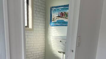 A small, narrow bathroom with a white toilet, a window, and a poster on the wall.