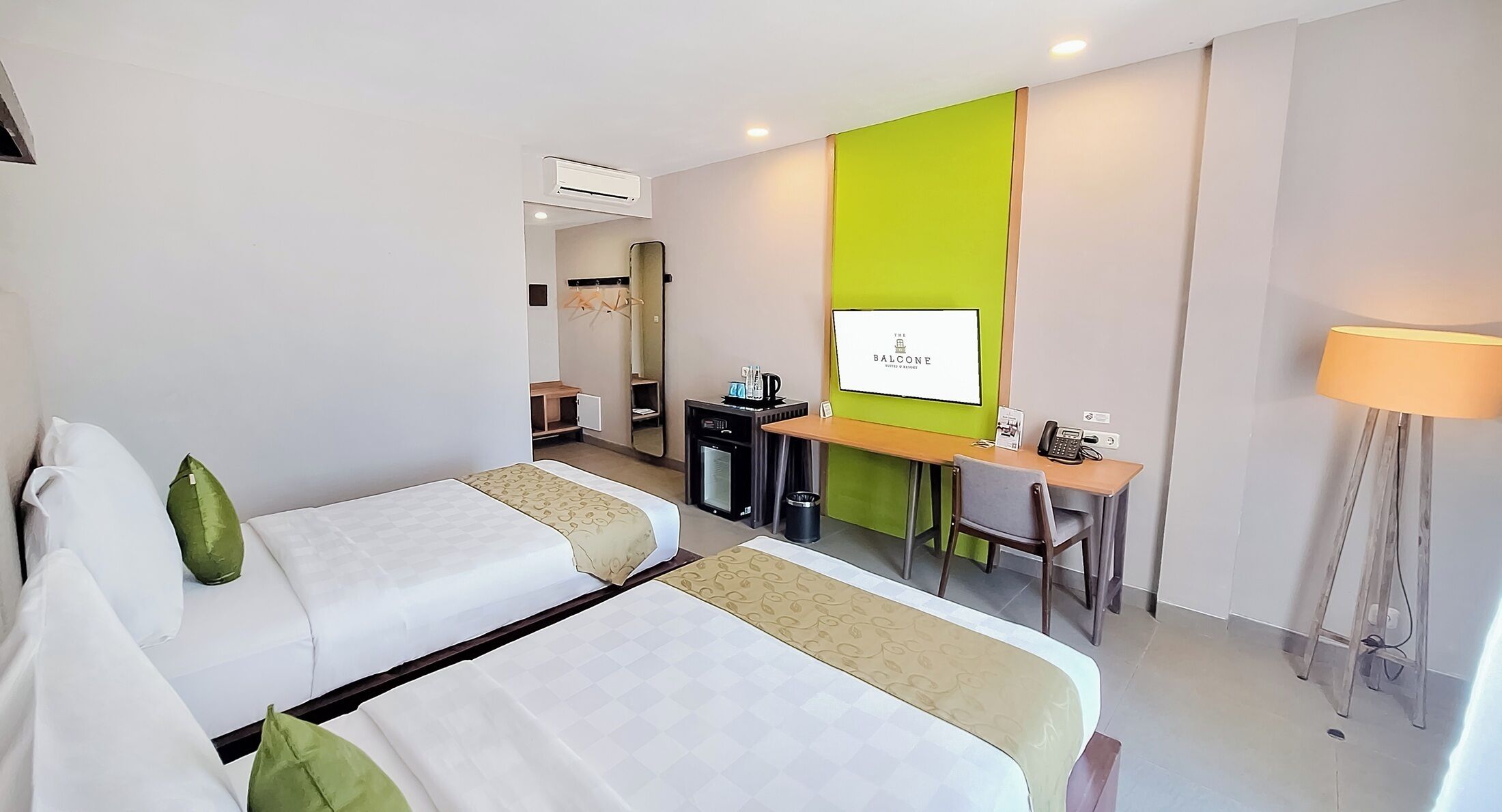 Een hotelkamer met twee bedden, een bureau, een spiegel, een kleine kitchenette en een groene accentmuur.
