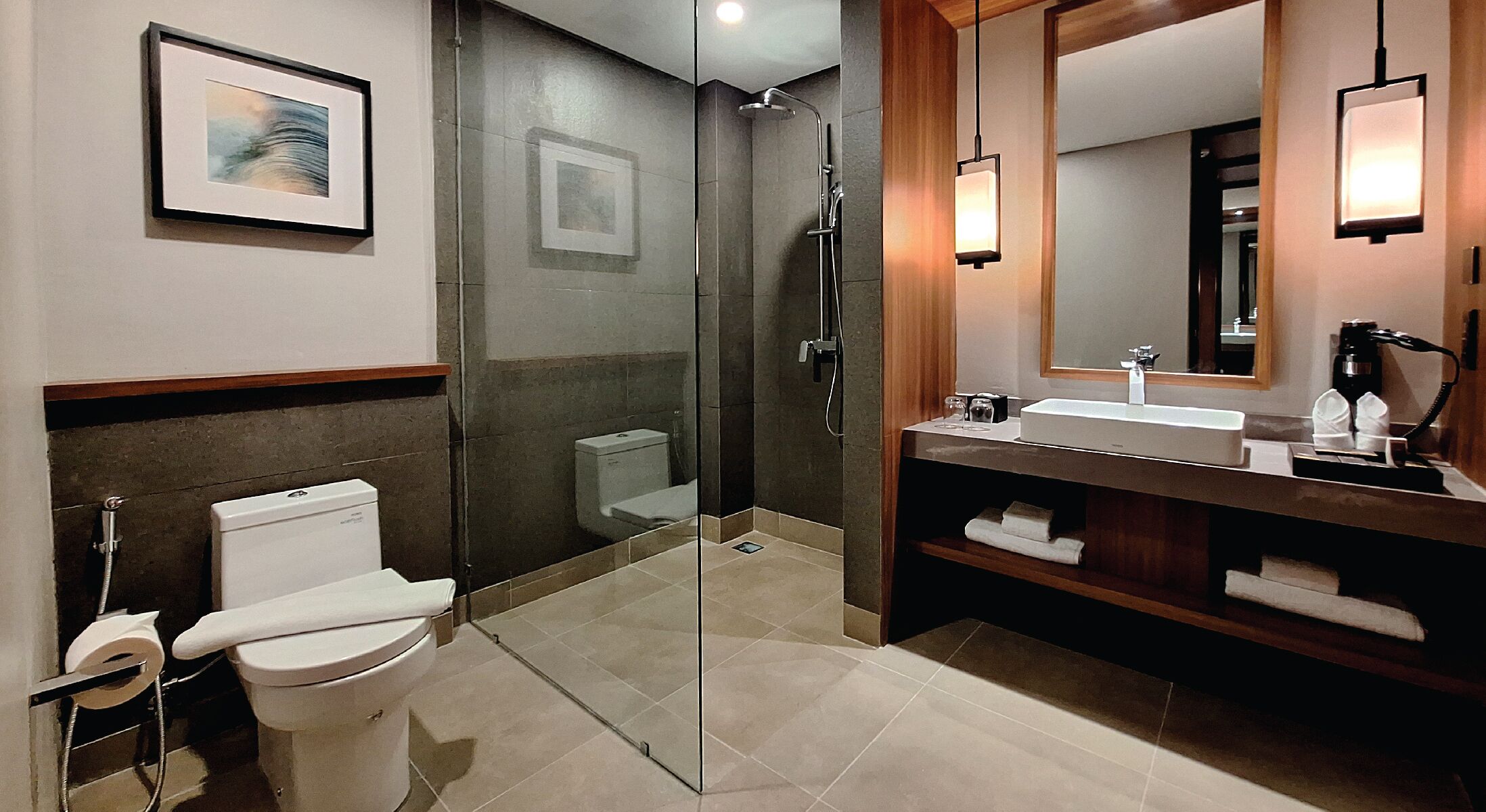A modern bathroom with a glass-enclosed shower, a white toilet, a sink with a mirror, and a framed picture on the wall.