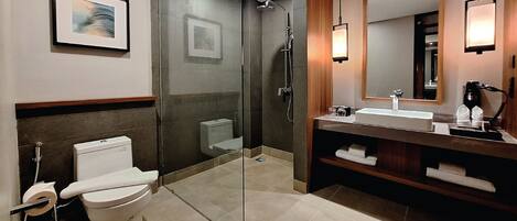 A modern bathroom with a glass-enclosed shower, a white toilet, a sink with a mirror, and a framed picture on the wall.