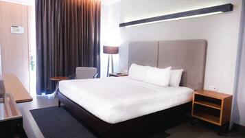 A hotel room with a large bed, a desk, a chair, and a nightstand.