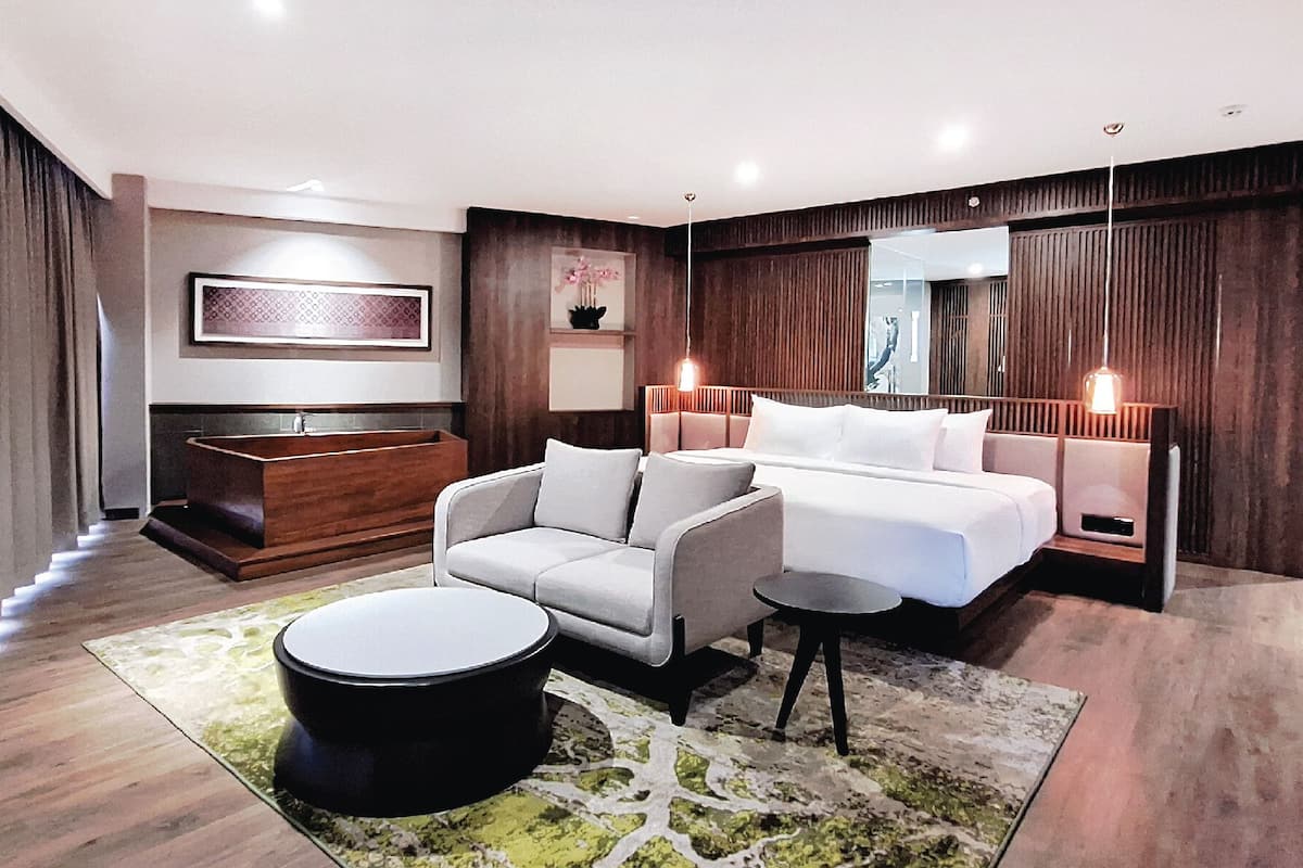 Moderni hotellihuone, jossa on suuri sänky, sohva, pyöreä sohvapöytä ja puinen kylpyamme.