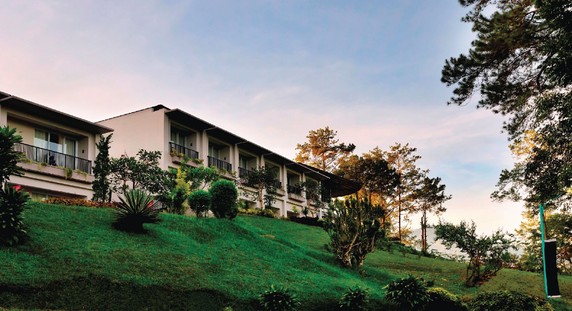 A multi-story hotel with balconies, surrounded by greenery and trees.