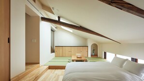 A modern bedroom with a large bed, wooden flooring, a dining area with a table and chairs, and a view of the kitchen in the background. - Enso Machiya (Kyoto)