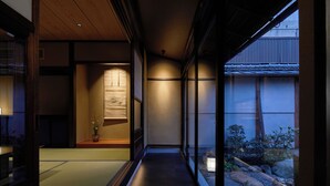 A traditional Japanese interior with tatami flooring, sliding doors, and a view of a garden with rocks and plants. - Enso Machiya (Kyoto)