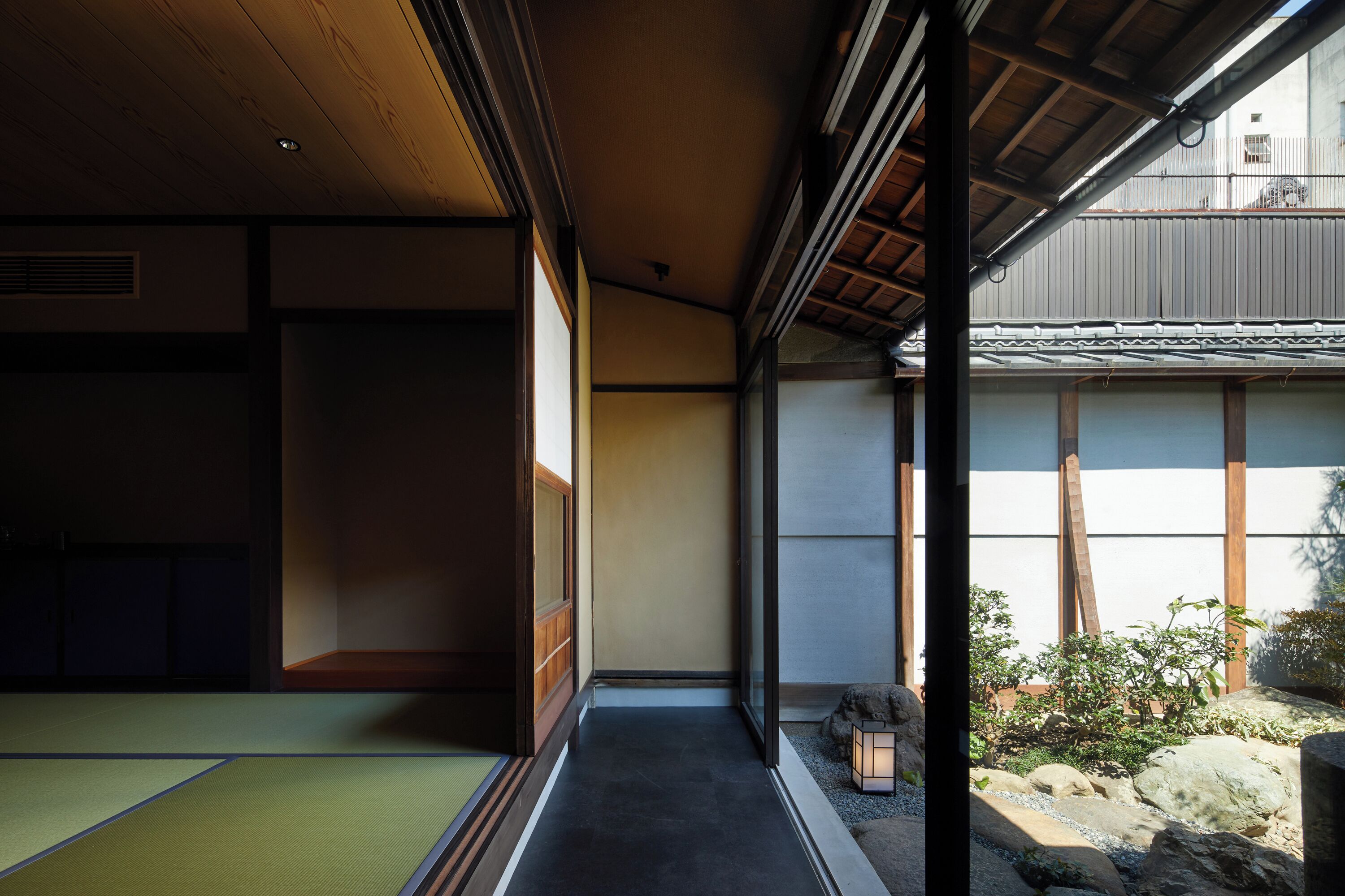 Une pièce de style japonais traditionnel, avec un sol recouvert de tatamis, des portes coulissantes et une vue sur un jardin agrémenté de rochers et d’une lanterne.