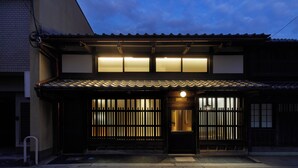 A traditional Japanese building with a tiled roof, wooden sliding doors, and illuminated windows. - Enso Machiya (Kyoto)