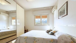 Un dormitorio con una cama, una ventana con persianas, un espejo y un aire acondicionado instalado en la pared.