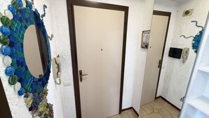 Un pasillo con una puerta blanca, un mosaico decorativo en la pared y un suelo de baldosas.