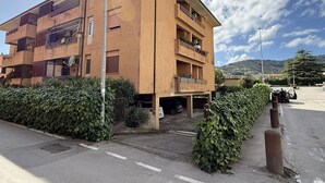 Un edificio residencial de varios pisos con balcones, un estacionamiento y cielo despejado.