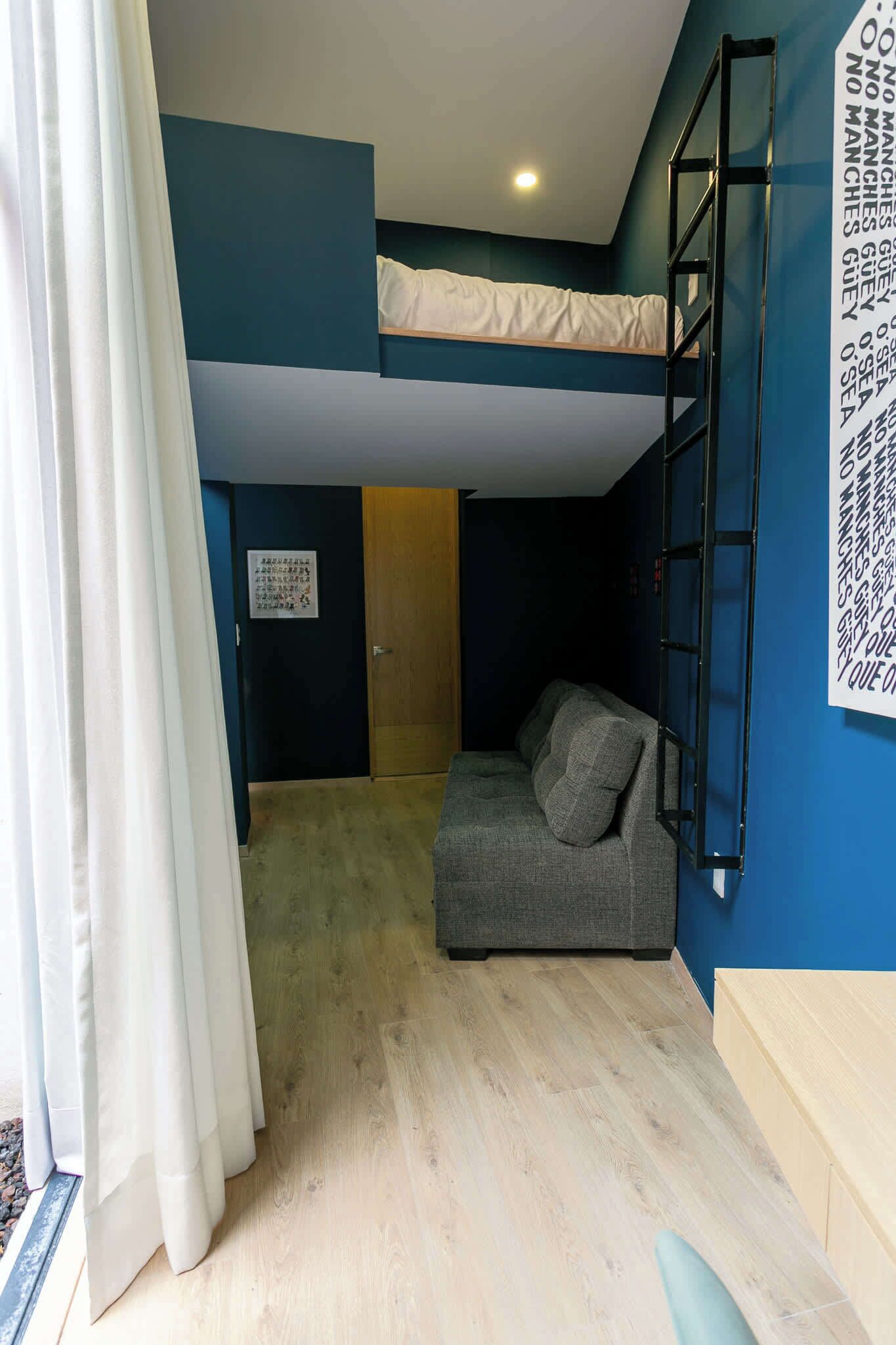 A room with a bunk bed, a sofa, a ladder, and a wall with text.