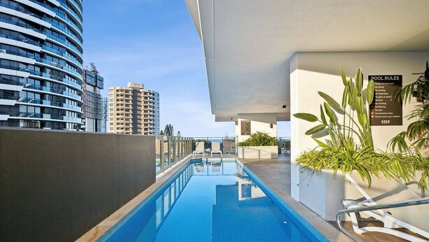 A modern hotel pool area with a clear view of the city skyline, including high-rise buildings. - Sun-Kissed Coastal Comfort | Pool•Gym•Beach•BBQ (Broadbeach)