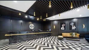 A modern reception area with a black and white herringbone floor, a marble reception desk, and a sofa. - Sun-Kissed Coastal Comfort | Pool•Gym•Beach•BBQ (Broadbeach)