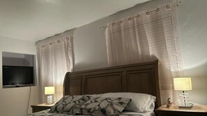 A bedroom with a bed, curtains, a TV, and bedside lamps. - Charming bungalow with AC and WiFi in serene Blainville
1 King size bedroom  (Blainville)