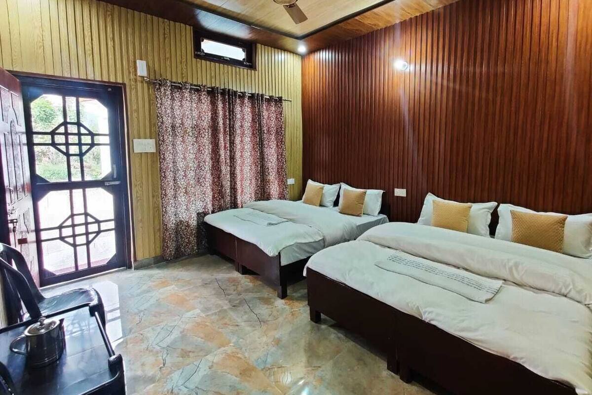 A room with two beds, a ceiling fan, a wooden wall, a window with curtains, and a door with a geometric design.