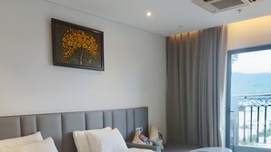 Ein Hotelzimmer mit zwei Betten, einem großen Fenster mit Ausblick, einem Deckenlüfter und einem gerahmten Kunstwerk an der Wand.