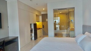 Ein modernes Hotelzimmer mit einem großen Bett, einem Schreibtisch, einer Küchenzeile und einer Schiebetür zu einem Badezimmer.