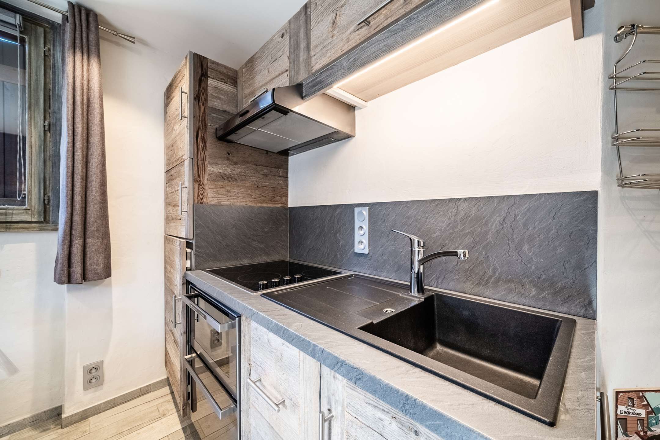 A modern kitchen with a double sink, stove, oven, and a wooden accent wall.