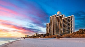 A high-rise hotel with multiple floors, located on a beach with a view of the ocean.