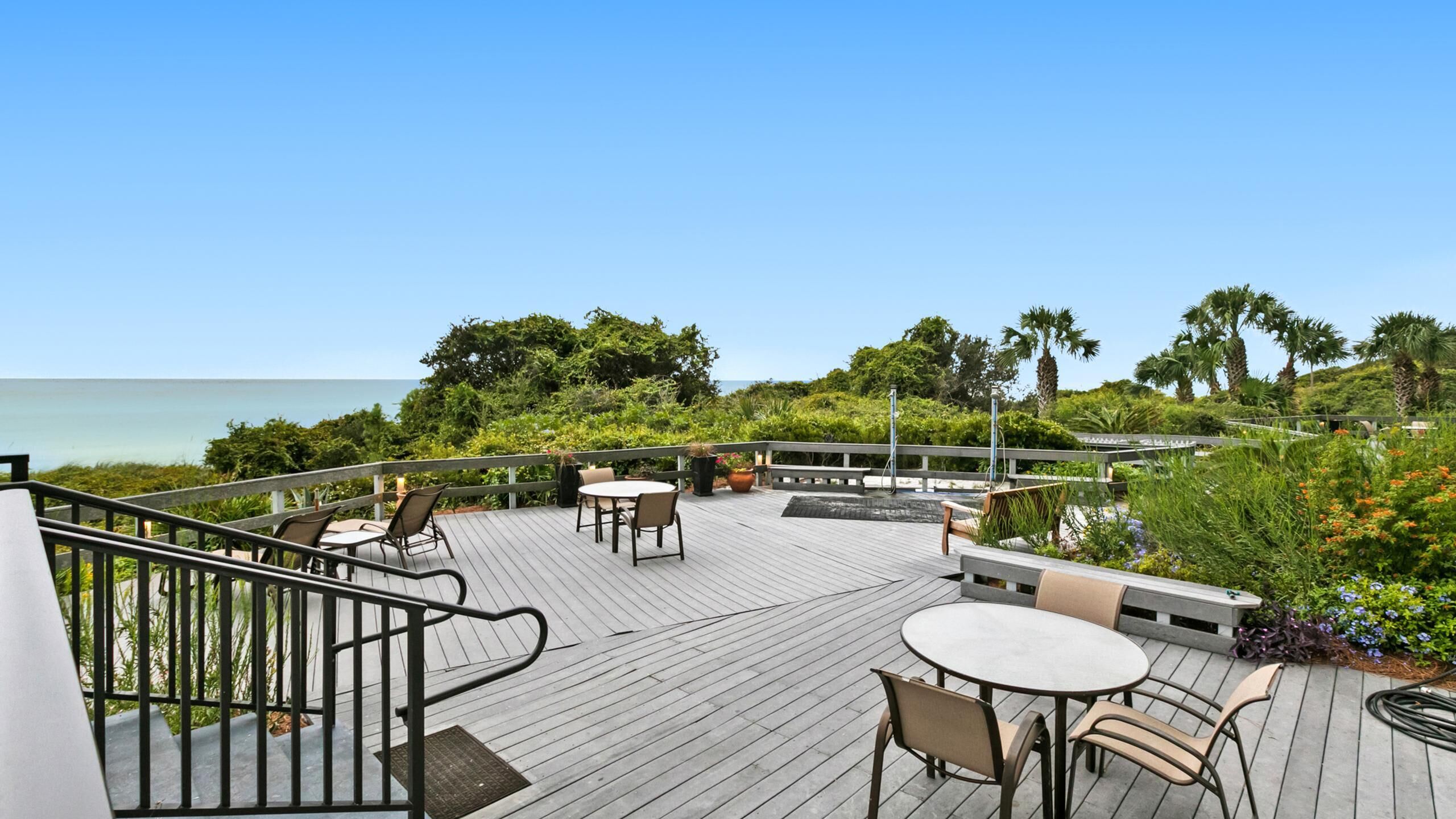 A wooden deck with outdoor seating, overlooking a body of water and lush greenery.