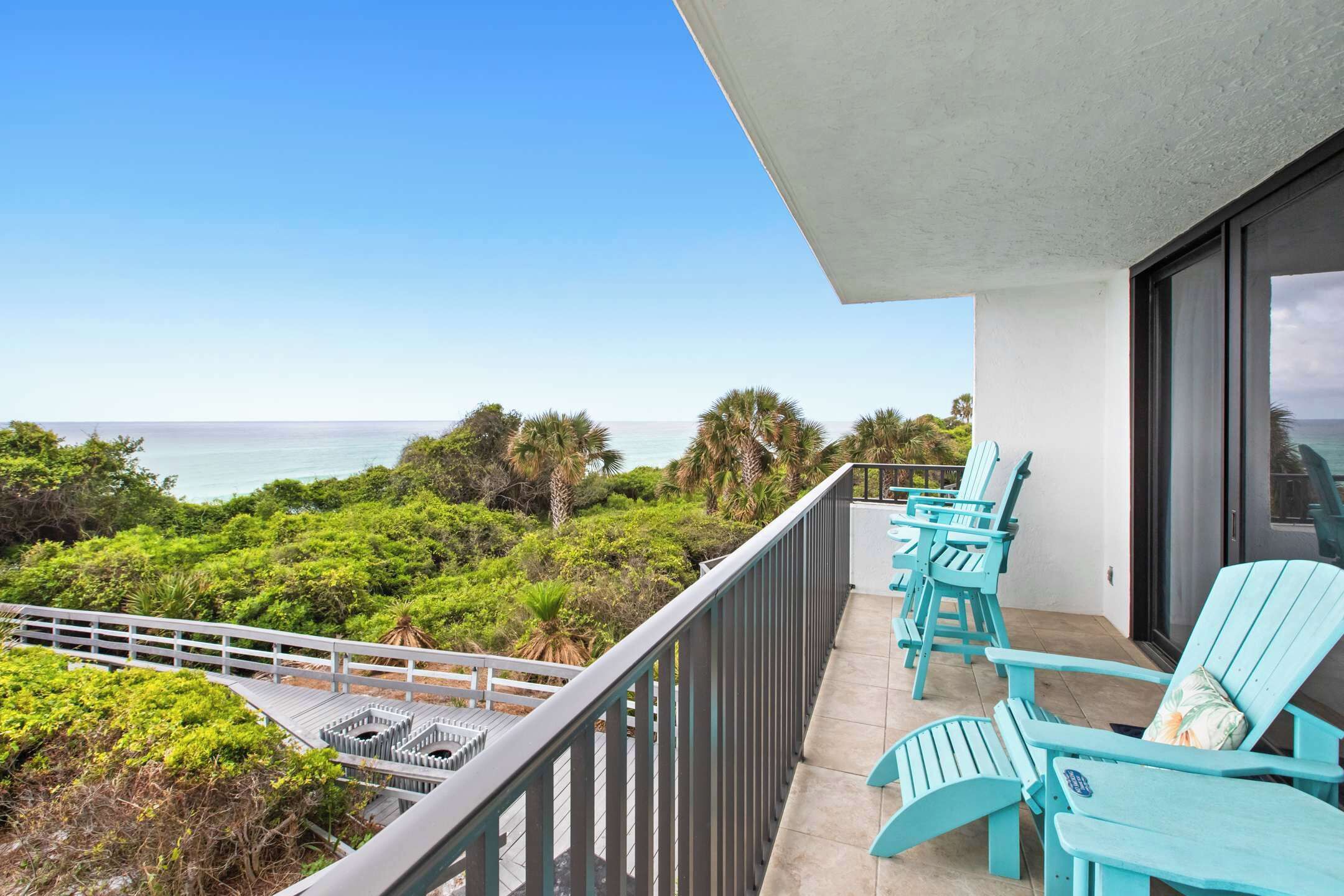 A balcony with turquoise chairs overlooking a lush landscape and the ocean.
