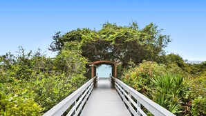 A wooden bridge leading to a natural area with dense foliage and a clear sky.